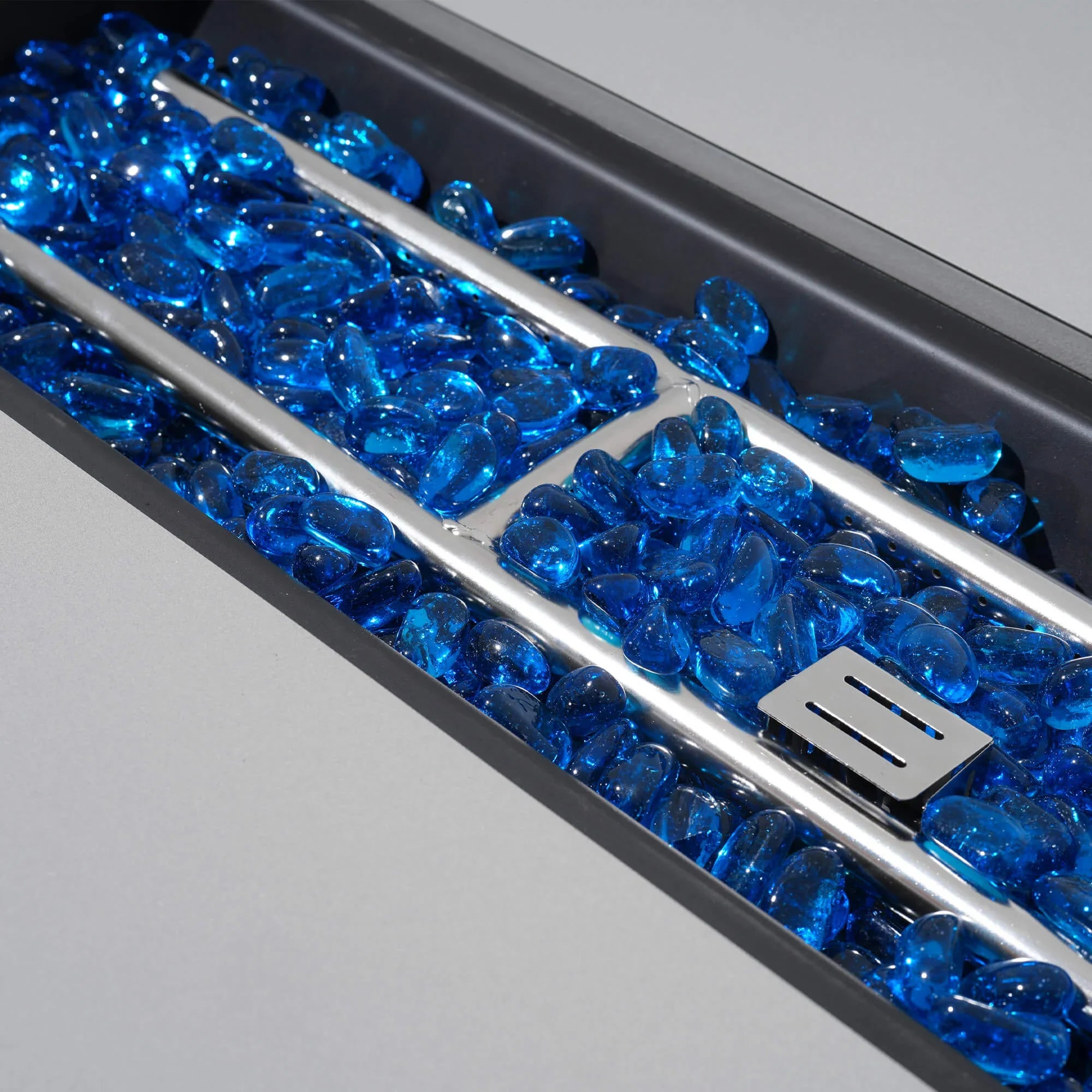 Close-up of a fire pit with blue glass stones and a metal grate