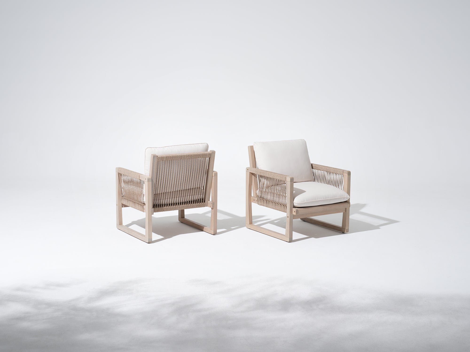 Two modern lounge chairs with woven frames and white cushions