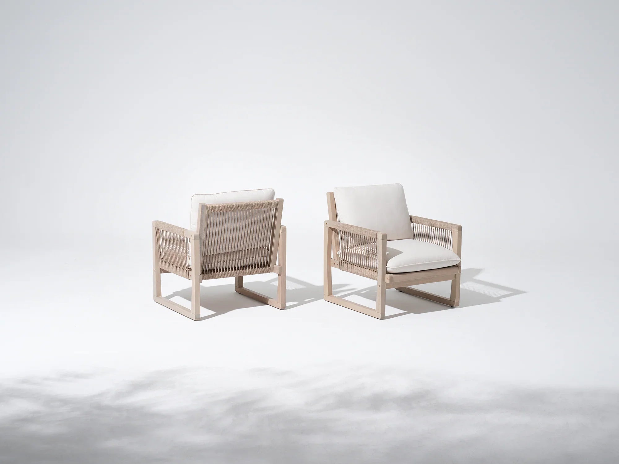 Two modern lounge chairs with woven frames and white cushions