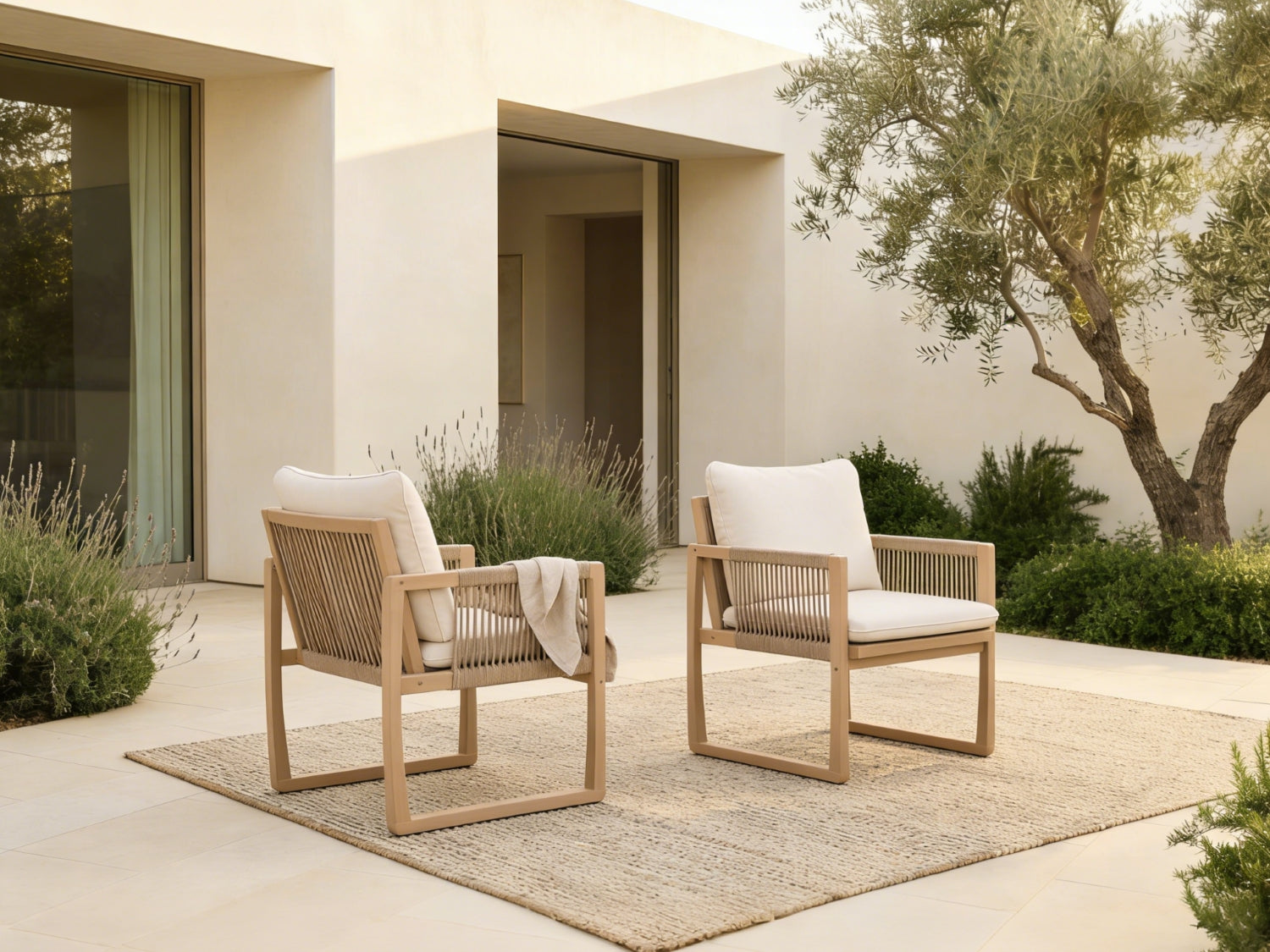 Two acacia wooden rope chairs with white cushions on a patio in front of a modern building - Jardina Premium Modern Outdoor Dining Furniture