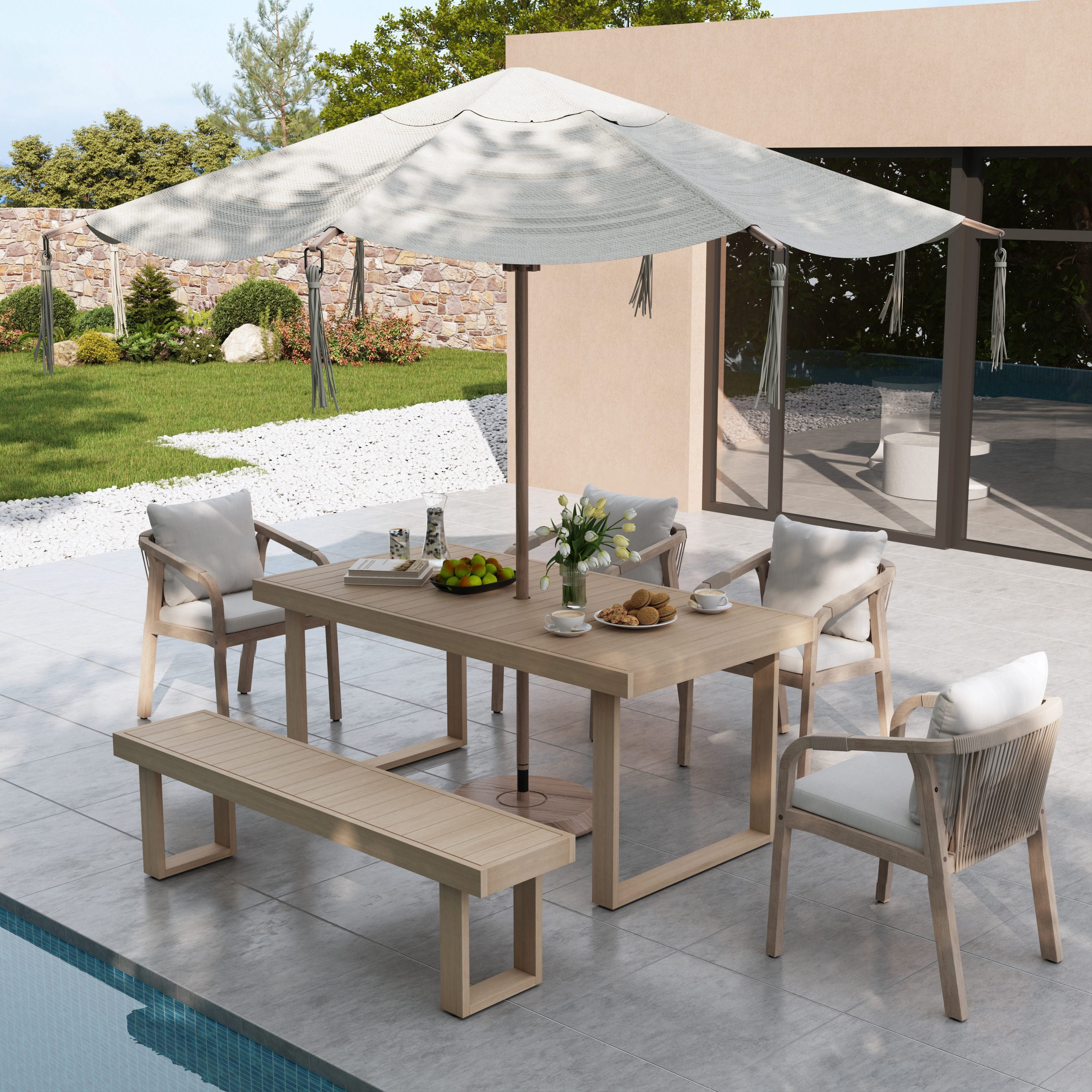Outdoor dining set with table, chairs, and bench under a large umbrella by a pool.