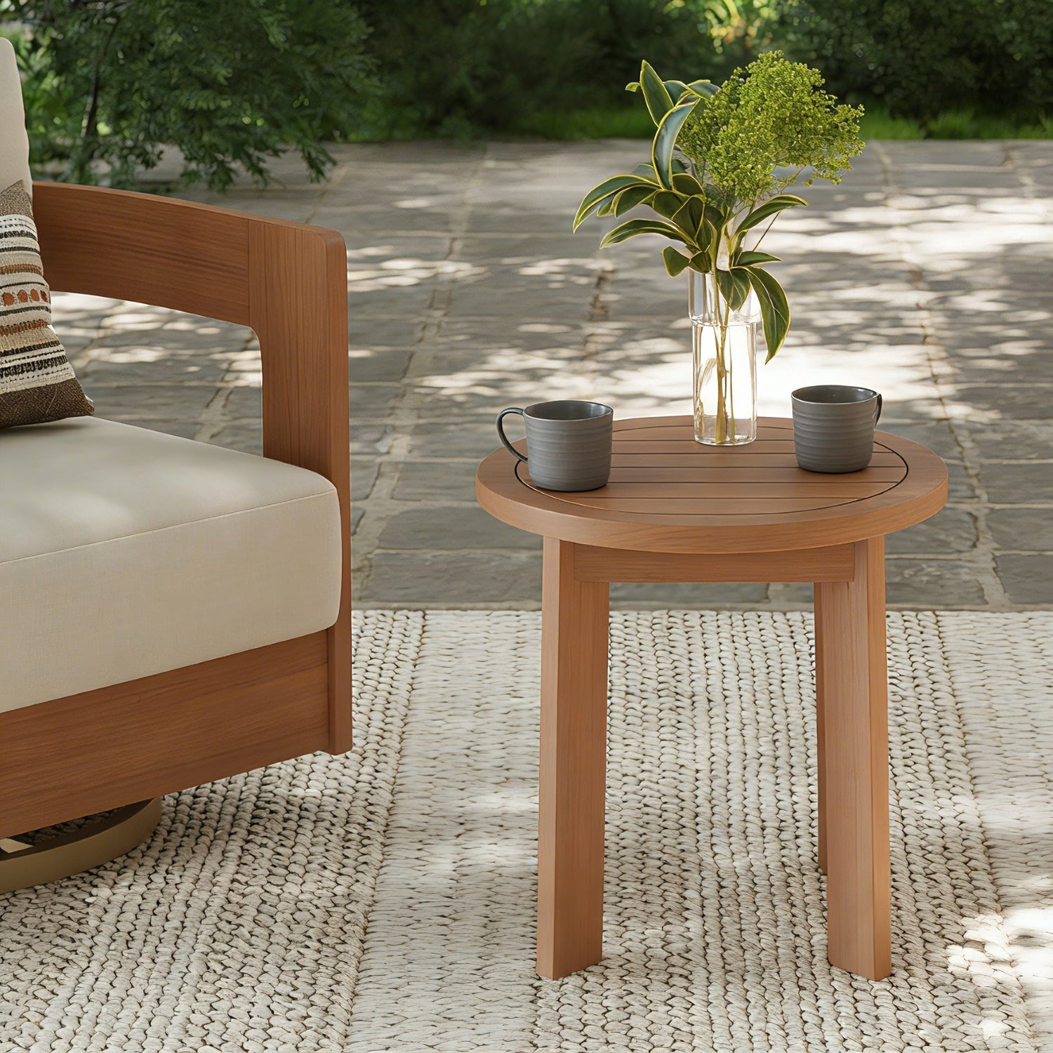 Wooden outdoor chair with a small round table featuring two cups and a vase of flowers, set on a stone patio.