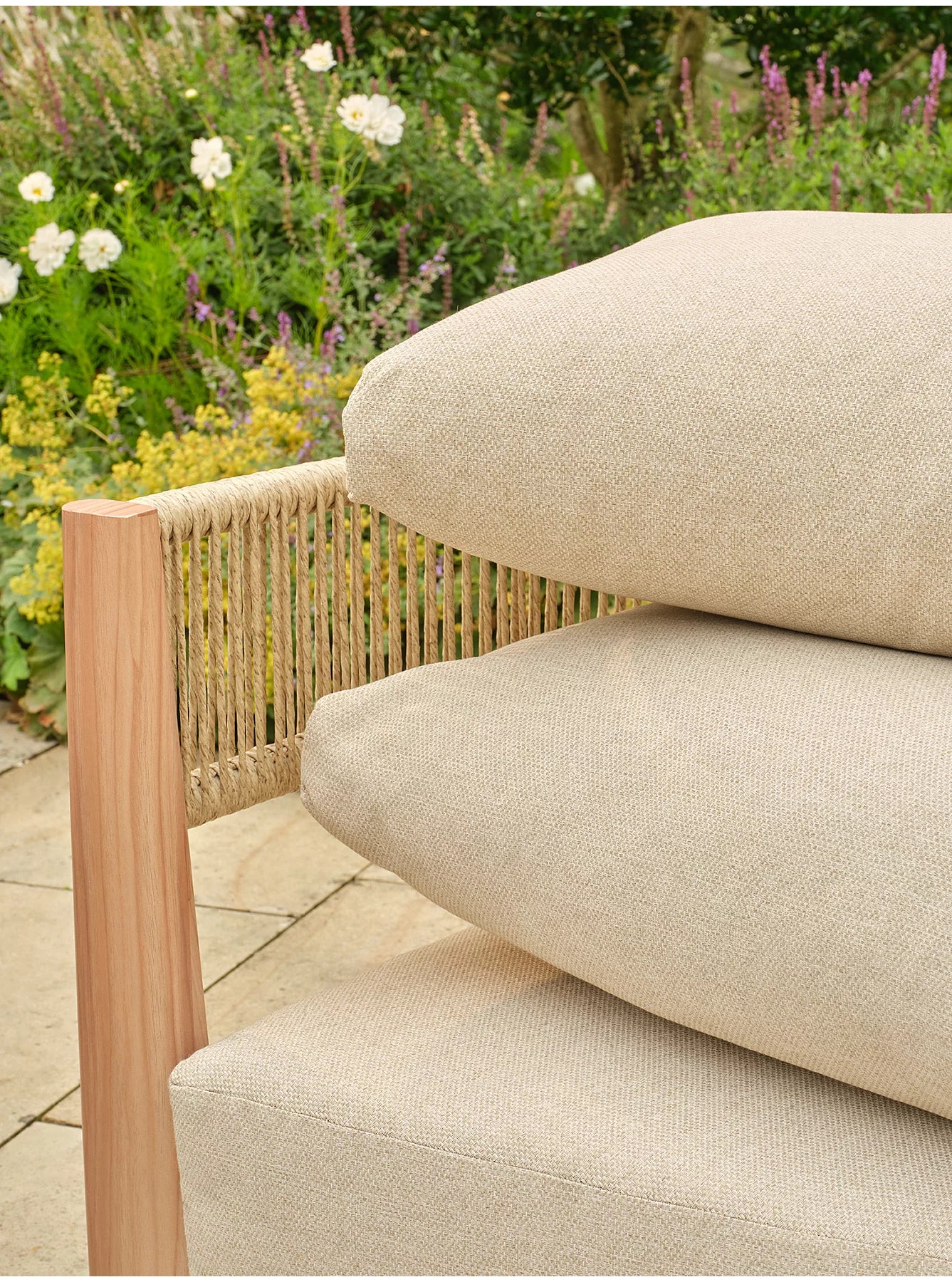 Close-up of a beige textured outdoor sofa cushion resting on a light wood and woven rope chair in a garden patio- Jardina outdoor modern premium patio furniture setting.