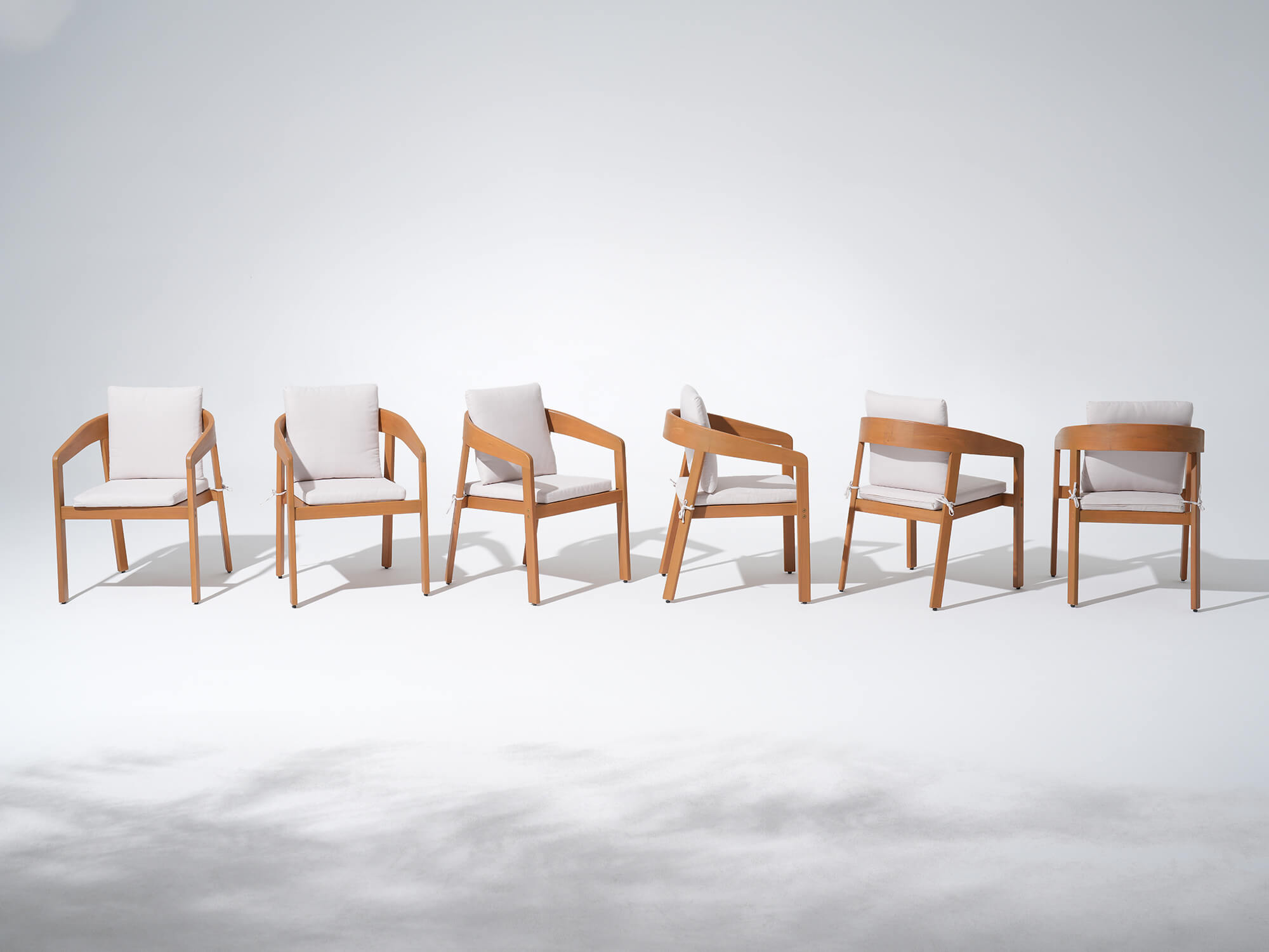 Six wucalyptus wooden dining chairs with white cushions arranged in a row - Jardina’s Modern Premium Outdoor Furniture