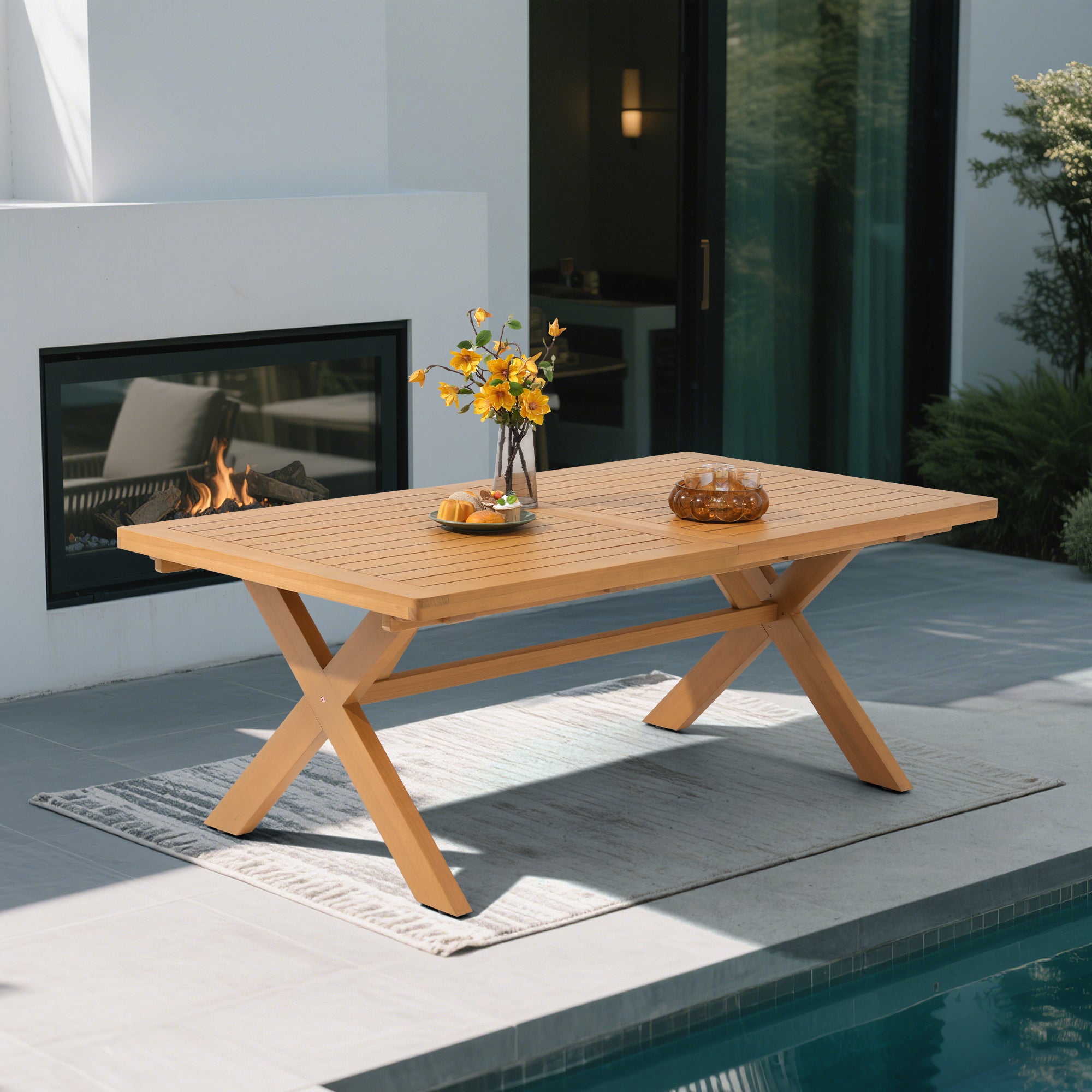Eucalyptus Wooden outdoor dining table with X-shaped legs in front of a fireplace  - Jardina’s Modern Premium Outdoor Furniture