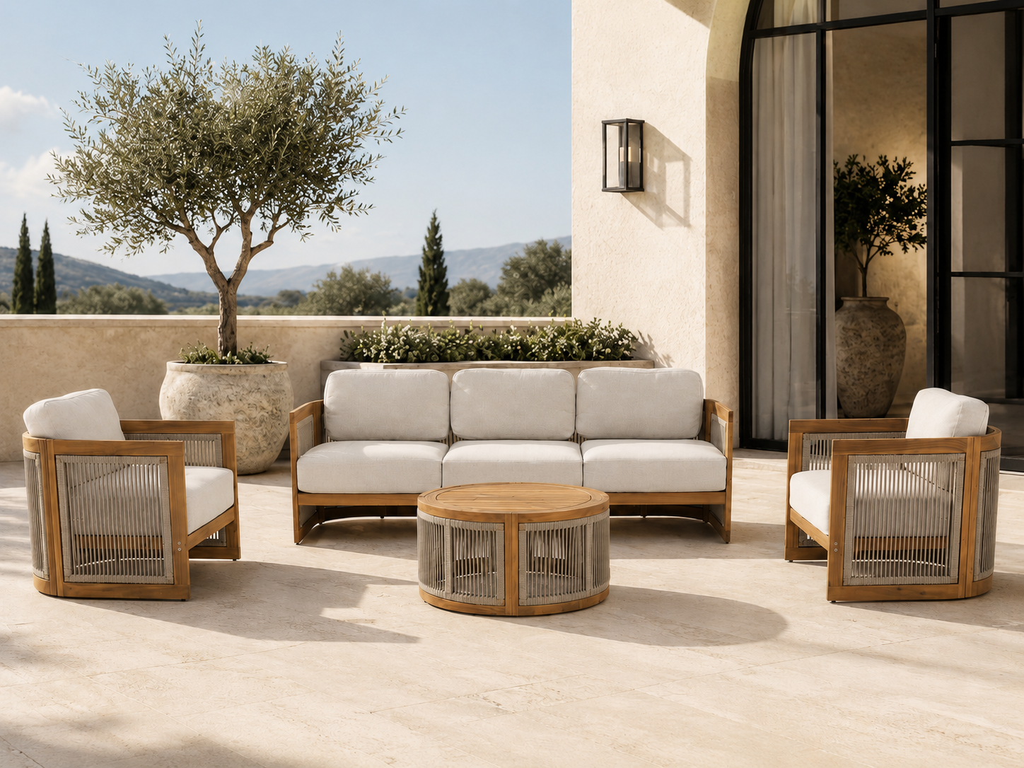 Outdoor patio furniture set with a three-seat sofa, two matching armchairs, and a round coffee table, all in light wood and off-white cushions, arranged on a stone patio with a stucco building and trees in the background. #Size_4-pc with Sofa