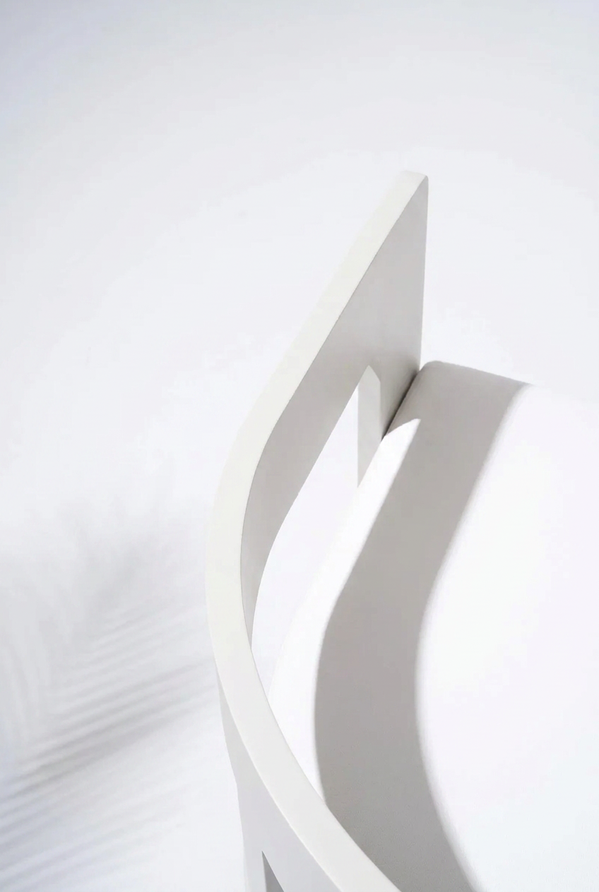 A close-up, high-angle view of a modern white chair with a curved backrest and minimalist design, set against a clean white background with soft shadows.